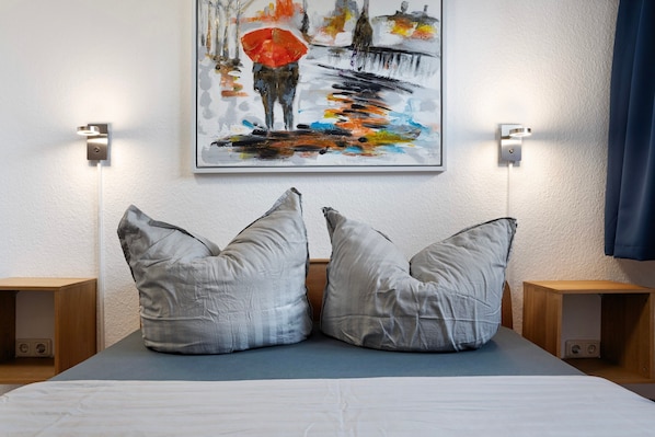 A bed with two pillows, a painting on the wall, and bedside tables with lamps.