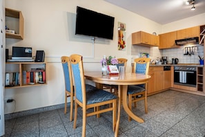A modern kitchen with wooden cabinets, a built-in oven, and a dining area with two chairs and a table.