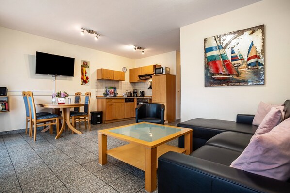 A modern living room with a sofa, a glass-top coffee table, and a dining area with chairs and a table.