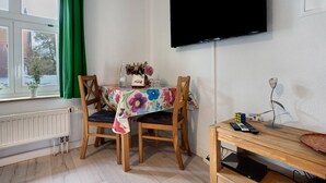A room with a dining table, chairs, a flat-screen TV, a radiator, and a window with curtains. - Studio Apartment 'Bäckerhus - Ferienwohnung 3' with Shared Terrace and Garden (Wiek)