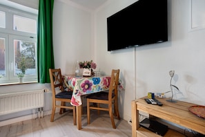 A room with a dining table, chairs, a flat-screen TV, a radiator, and a window with curtains.