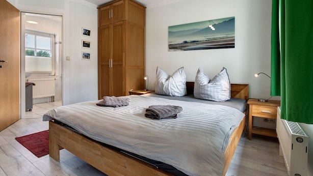 A bedroom with a bed, nightstands, a wooden wardrobe, a painting, and a radiator. - Studio Apartment 'Bäckerhus - Ferienwohnung 3' with Shared Terrace and Garden (Wiek)