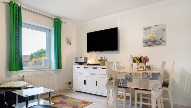 A modern room with a dining table, chairs, a TV, and a window with curtains. - Apartment 'Bäckerhus - Ferienwohnung 6' with Private Terrace, Shared Garden and Wi-Fi (Wiek)