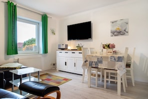 A modern room with a dining table, chairs, a TV, and a window with curtains.