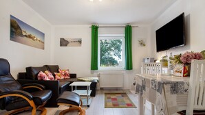 A living room with a sofa, chairs, a table, a TV, and a window with curtains. - Apartment 'Bäckerhus - Ferienwohnung 6' with Private Terrace, Shared Garden and Wi-Fi (Wiek)