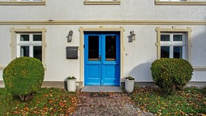 Un edificio con una puerta azul, dos plantas en macetas y un camino de ladrillo.