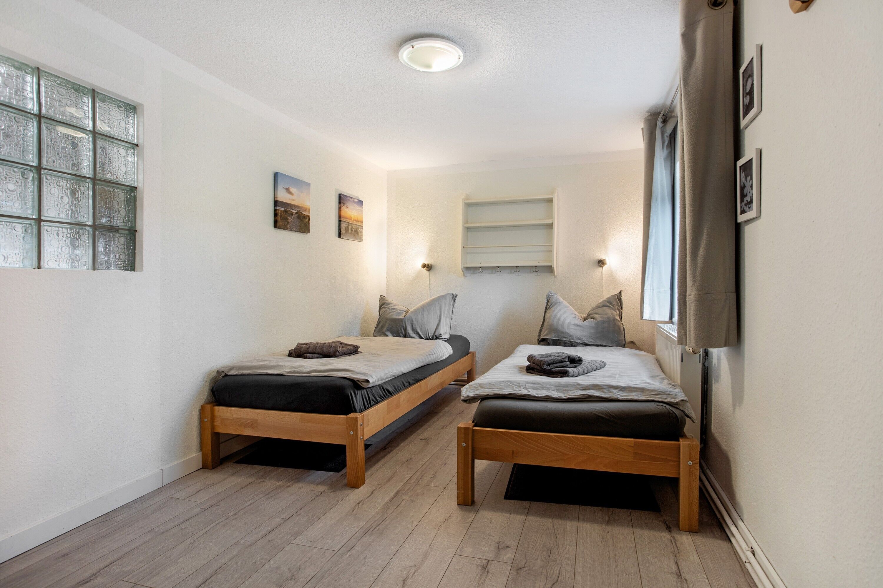 A room with two wooden beds, a window with frosted glass, and a shelf with pictures.