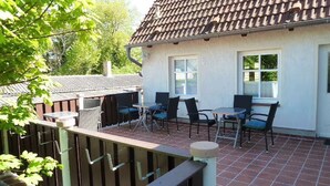 Un patio con mobiliario exterior, techo de baldosas y pared blanca.