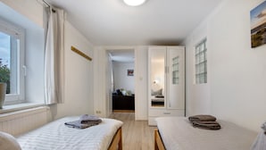 Un dormitorio con dos camas, una ventana, un radiador y una puerta que da a otra habitación.