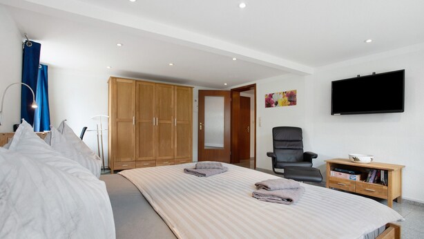 Een slaapkamer met een bed, een stoel, een televisie en een kledingkast.