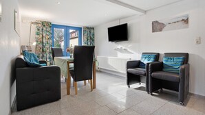 Een moderne woonkamer met een eethoek, twee relaxfauteuils, een flatscreen televisie en een raam met gordijnen.