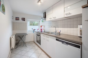 Une cuisine moderne avec des meubles blancs, un lave-vaisselle et une fenêtre équipée de stores.