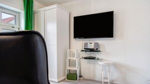 Un soggiorno moderno con una TV a schermo piatto, un armadio bianco, un piccolo tavolino e un contenitore portaoggetti verde.