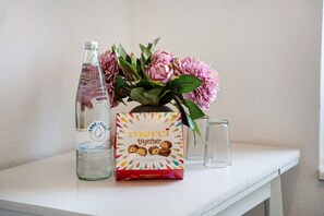 A bottle, a box of chocolates, and a vase with flowers on a white surface.