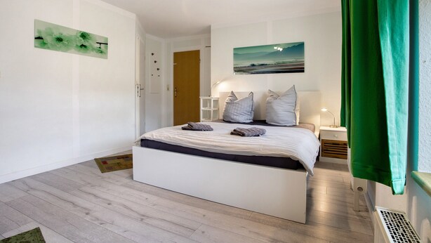 Una camera da letto con un letto, un comodino, una lampada, una tenda verde e un quadro appeso al muro.