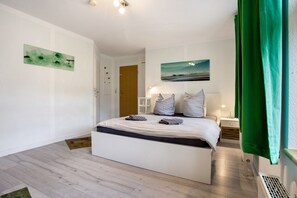 A bedroom with a bed, a nightstand, a lamp, a green curtain, and a painting on the wall. - Studio Apartment 'Bäckerhus - Ferienwohnung 5' with Terrace, Shared Garden and Wi-Fi (Wiek)