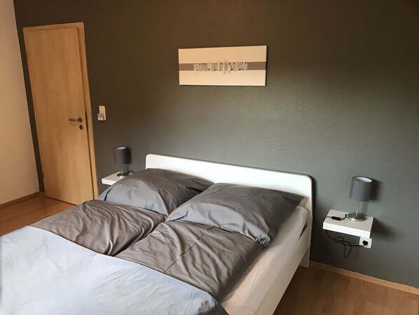 A bedroom with a bed, two bedside tables, a wall-mounted light, and a door.