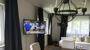 Una sala de estar moderna con comedor, televisor de pantalla plana en la pared, candelabro y un sofá con cojines.
