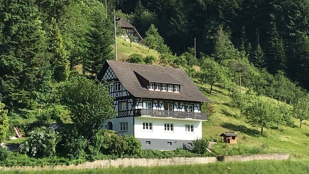 Una casa de dos pisos con un techo empinado, rodeada de un bosque denso.