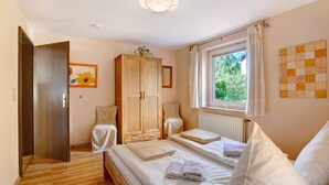 Un dormitorio con armario de madera, cama con ropa de cama blanca, ventana con cortinas y radiador.
