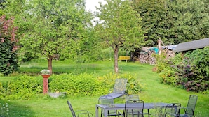 Un jardín con mesa y sillas, rodeado de follaje y árboles.