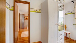 Una habitación con suelo de madera, un armario blanco con cajones, un espejo y una silla.