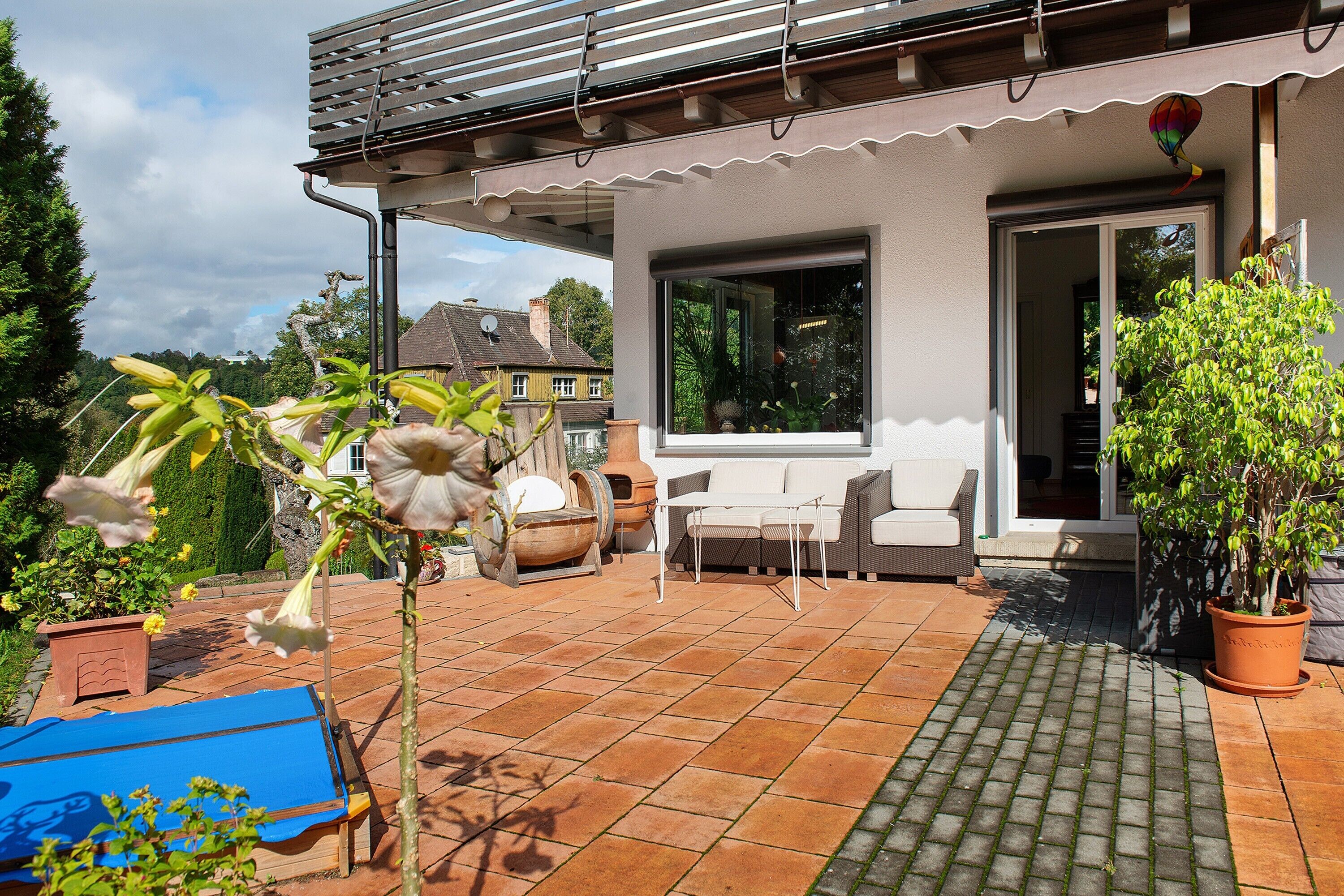 A patio with a table and chairs, a potted plant, and a large window.