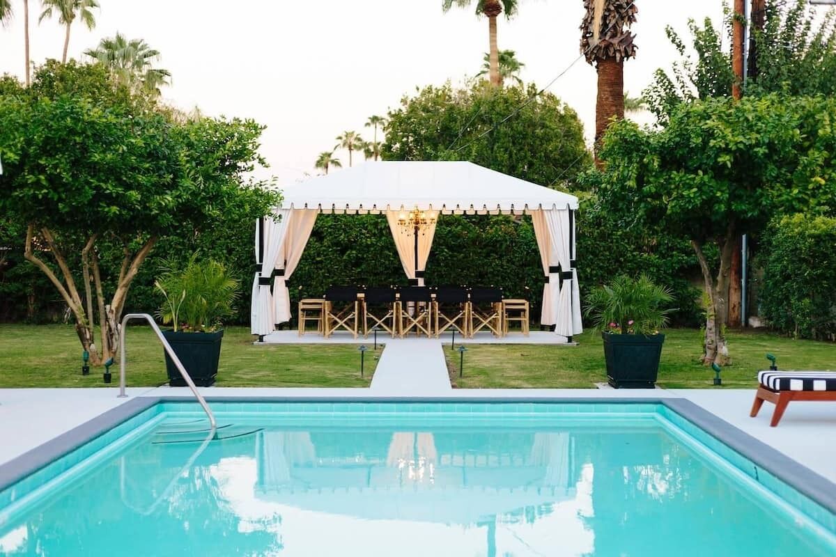 Un espace aménagé au bord de la piscine, avec un auvent blanc, des sièges et une piscine.