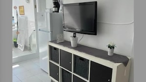 A modern living room with a flat-screen TV mounted on the wall, a white console table with black storage drawers, and a small potted plant. - Sea view studio with balcony, 2 steps from the beach (Mogán)