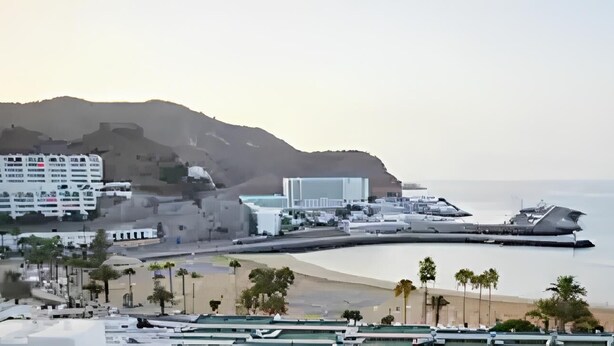 A coastal cityscape with a beach, buildings, and a hilly background. - Sea view studio with balcony, 2 steps from the beach (Mogán)
