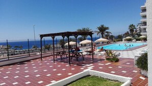 A rooftop pool area with a pergola, lounge chairs, and umbrellas. - Sea view studio with balcony, 2 steps from the beach (Mogán)