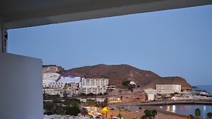 A coastal cityscape with buildings, a mountain, and a body of water. - Sea view studio with balcony, 2 steps from the beach (Mogán)