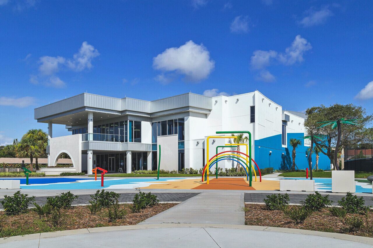 Un bâtiment moderne doté d’une grande entrée, d’une aire de jeux avec des équipements colorés et d’un ciel d’un bleu éclatant.