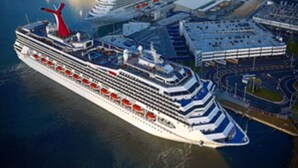 Een groot cruiseschip afgemeerd in een haven, met meerdere dekken en een opvallende rode schoorsteen.