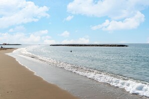 Ein Strand mit ruhigen Wellen, einer entfernten Felsformation und einem klaren Himmel.