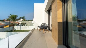 A balcony with a glass railing, a cushioned chair, and a view of neighboring buildings. - Sunny Villa by Platja Ardiaca (Cambrils)