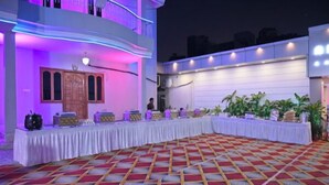 Een feestzaal met een lange tafel gedekt voor een maaltijd, omringd door een betegeld tapijt en een balkon met paarse verlichting.