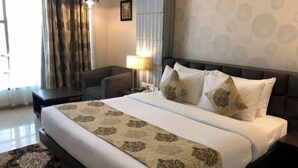 Een hotelkamer met een groot bed, een bureau, een stoel, een lamp en een kamerbreed tapijt met dessin.