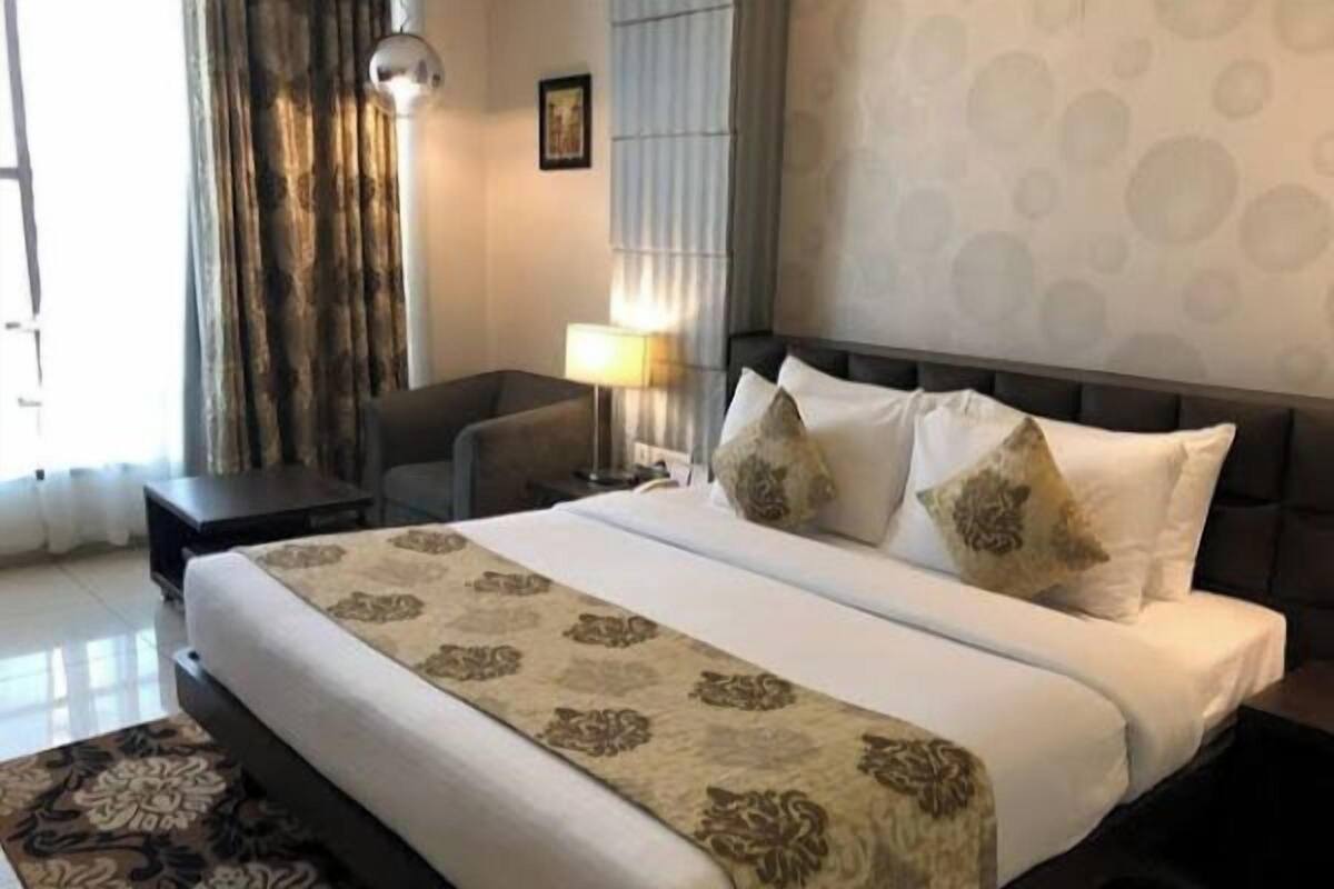 A hotel room with a large bed, a desk, a chair, a lamp, and a patterned rug.
