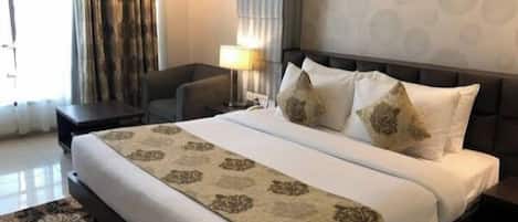 A hotel room with a large bed, a desk, a chair, a lamp, and a patterned rug.
