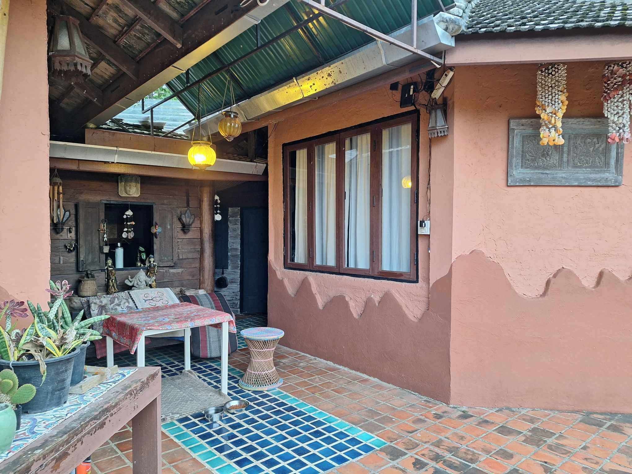 Eine gemütliche Terrasse im Freien mit einem Holztisch und Stühlen, einem kleinen runden Tisch und Blumentöpfen.