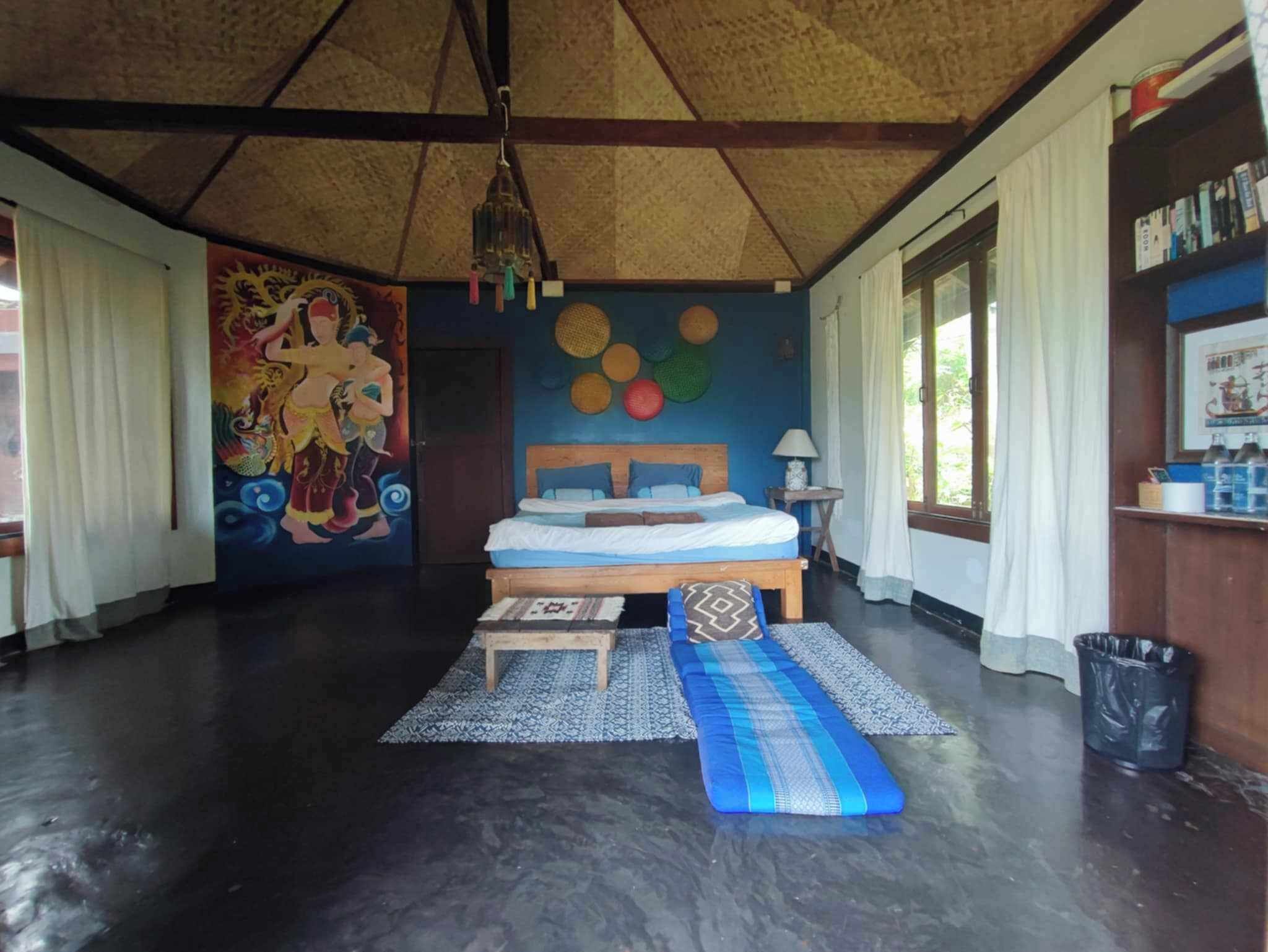 A room with a bed, a large mural, a ceiling fan, and a window with curtains.