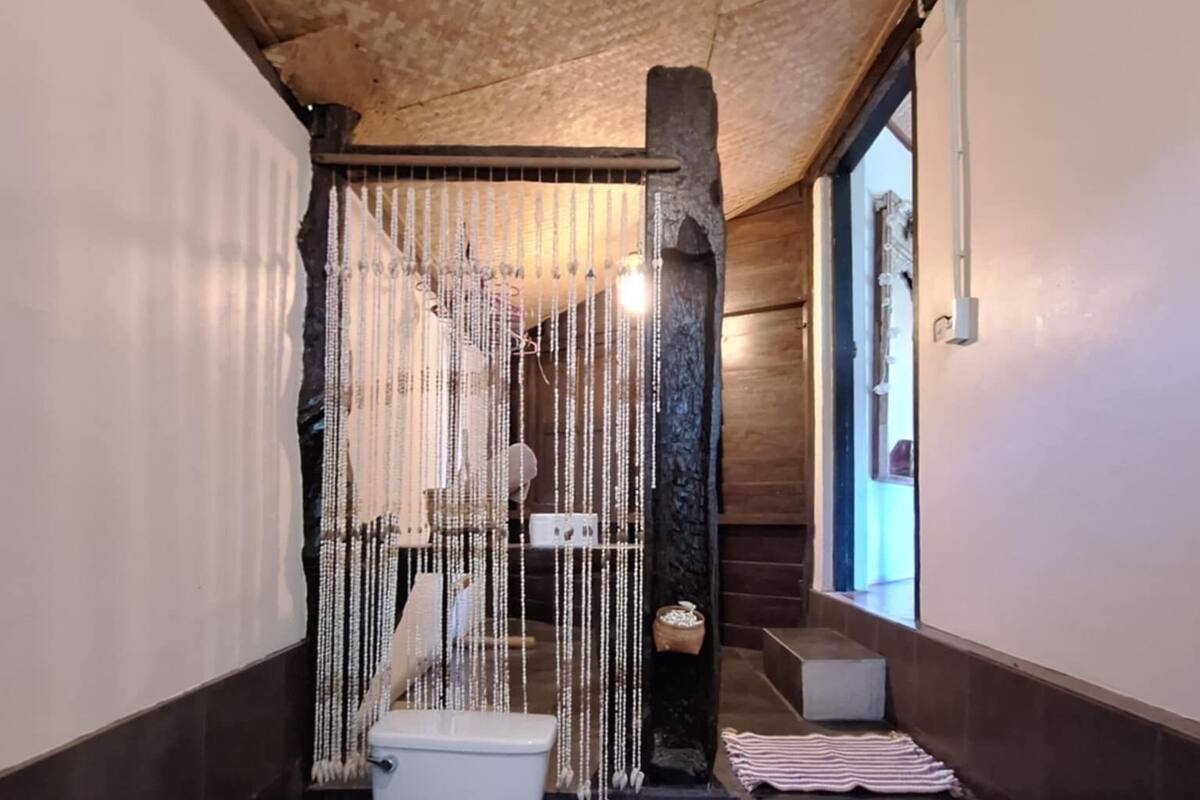Un baño pequeño y estrecho con inodoro, lavabo y zona de ducha. Cuenta con techo de madera y pared de piedra.