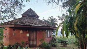 A rustic house with a tiled roof, surrounded by lush greenery and a stone pathway leading to a bench. - The Lookout Pai (Pai)