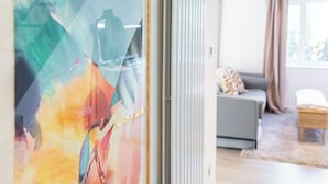 Un salón moderno con un sofá gris, una mesita de mimbre y vistas a través de un ventanal con arte abstracto.