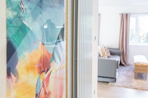 Un salón moderno con un sofá gris, una mesita de mimbre y vistas a través de un ventanal con arte abstracto.