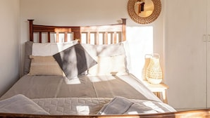 Una cama bien hecha con tablero de madera, una mesita de noche con un farol y un espejo redondo en la pared.