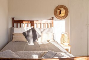Una cama bien hecha con tablero de madera, una mesita de noche con un farol y un espejo redondo en la pared.