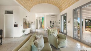 A spacious living area with a high ceiling, a sofa set, a dining area, and large sliding glass doors leading to an outdoor patio. - 4134 Villa Majer by Perle di Puglia (Manduria)