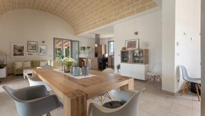 A spacious living area with a wooden dining table, modern chairs, and a kitchen in the background. - 4134 Villa Majer by Perle di Puglia (Manduria)